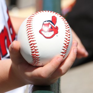 Child's hand holding a baseball with the Cleveland Indians logo, waiting for a player to sign it